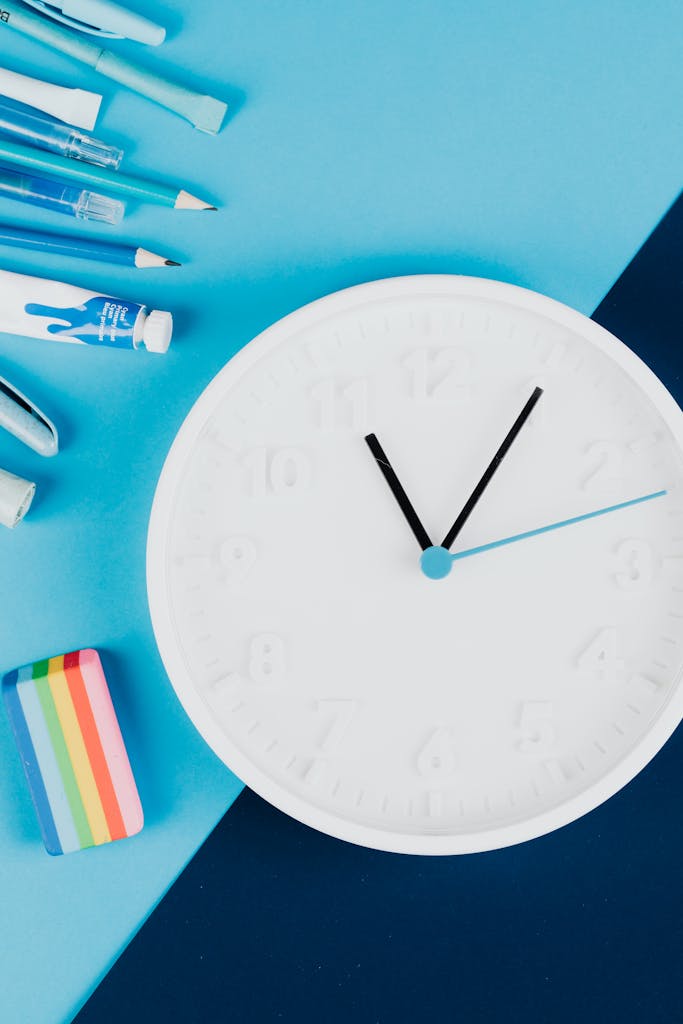 Flat lay of school supplies and a clock on a vibrant blue background.